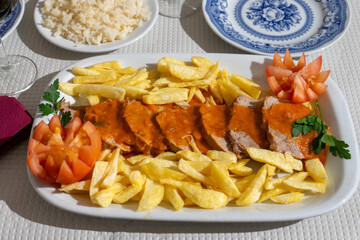 A plate of veal stew in a rich tomato sauce, served with crispy fries, is presented on a table at a traditional Alentejo restaurant. The rustic setting and hearty dish create a inviting atmosphere.