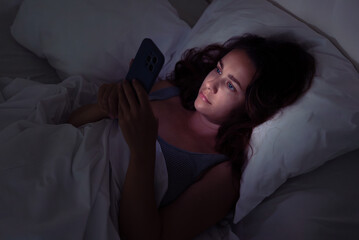 In the silent night, a woman lies in bed, drawn to her phone's glow, a scene illustrating the grip...