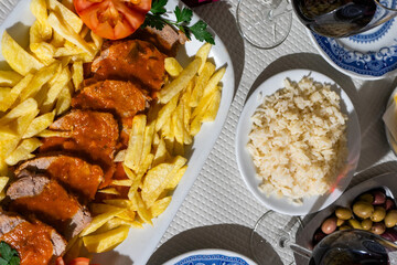 A plate of veal stew in a rich tomato sauce, served with crispy fries, is presented on a table at a traditional Alentejo restaurant. The rustic setting and hearty dish create a inviting atmosphere.