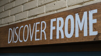 Close up of a wooden sign with discover frome against an old brick wall painted white in the market town of Frome in Somerset, UK