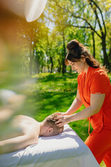 A master masseur in a bright orange uniform gives a healing body massage to a handsome man with...