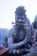 Portrait of an young male artist with painted face and bone in his mouth act as a demon during the masan holi festival at harishchandra ghat in Varanasi, India.