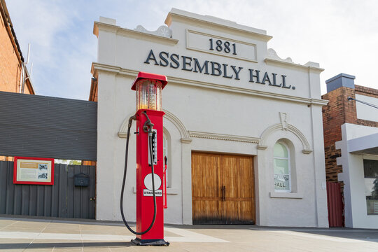 Low angle view of an old fashioned red petrol bowser in front of an historic assembly hall