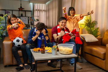 Group of Asian people friends sit on sofa watching and cheering football or soccer games...