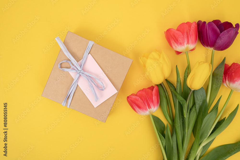 Wall mural Craft envelope tied with blue ribbon beside multicolored tulips on yellow background