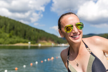 Young smiling woman near the mountain lake in the summer