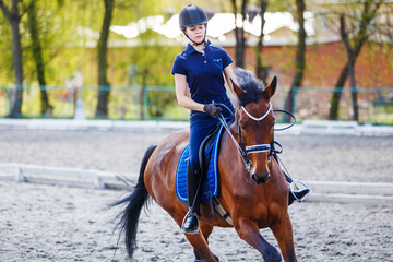 Young girl riding bay horse on equestrian dressage training