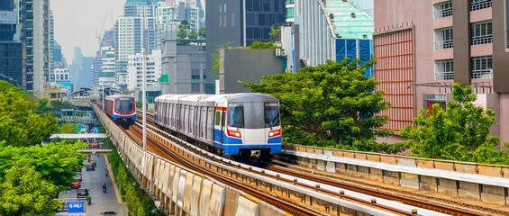 Modern subway electric train over ground on a bridge on stilts among skyscrapers metro with turn...