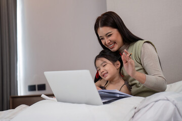 Mother and daughter lying in bed with on and smiling. Young mom working from home in bedroom with laptop