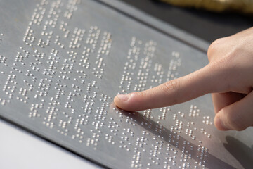A blind person pointing at a Braille sign on steel board.