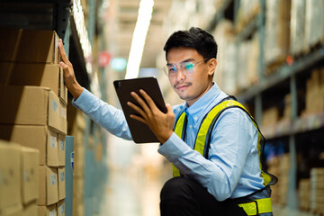 A man in a yellow vest is looking at a tablet while standing in a warehouse. He is focused on the...