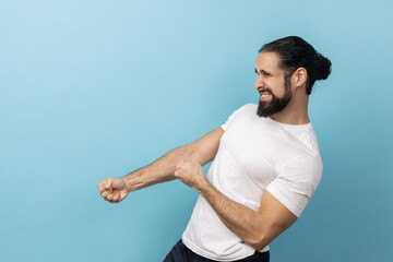 Side view portrait of handsome man with beard wearing white T-shirt standing in attack or pulling...