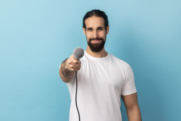 Portrait of man with beard wearing white T-shirt holding microphone, making interview and asking...