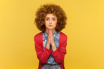 Portrait of pleading woman with Afro hairstyle holding hands folded in praying gesture, asking for...