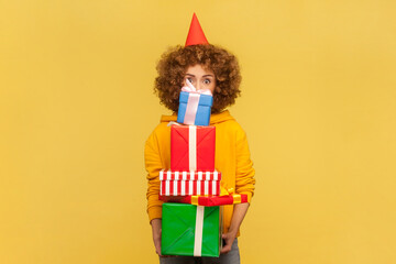 Portrait of astonished shocked woman in party with Afro hairstyle holding stack of presents, heavy...