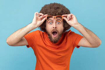 Shocked amazed man with Afro hairstyle wearing orange T-shirt standing and looking at camera,...