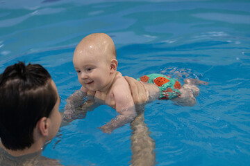 Smiling baby in the fun swim panties looking to the swim coach. Swimming lessons for newborn.