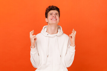 Portrait of hopeful young man wearing white hoodie crossed finger with hope, hopes dreams come...
