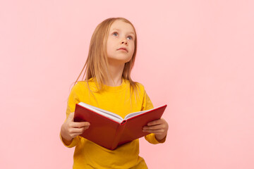 Portrait of dreaming blonde little girl holding book, looking away, dreaming, do not want to study,...