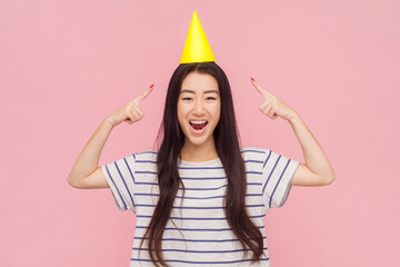 Portrait of festive amazed woman with long brunette hair celebrating birthday pointing at yellow...