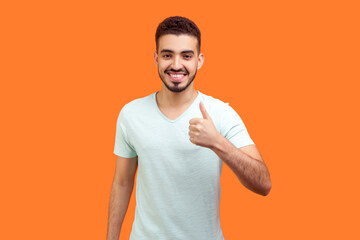 Portrait of smiling handsome young bearded man wearing T-shirt standing showing thumb up like...