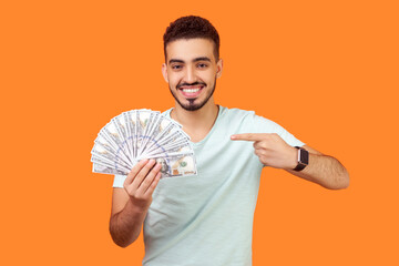 Portrait of smiling satisfied attractive young bearded man wearing T-shirt holding dollar banknotes...