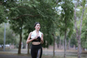 Young Asian woman running hard on the street at the park after daily exercise. Jogging to keep fit on a warm summer morning.