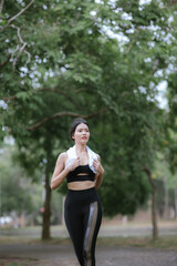 Young Asian woman running hard on the street at the park after daily exercise. Jogging to keep fit on a warm summer morning.