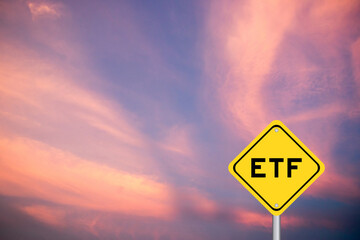 Yellow transportation sign with word ETF (abbreviation of Exchange Traded Fund) on violet color sky...