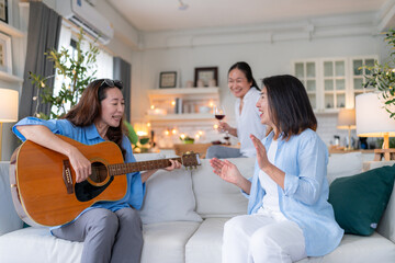 asian adult woman friend gathering having fun together while singing and playing the guitar at home. Friendship, reunion fun party home entertainment and people celebrate festive concept 