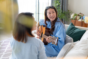 asian adult woman friend gathering having fun together while singing and playing the guitar at home. Friendship, reunion fun party home entertainment and people celebrate festive concept 