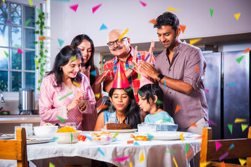 Indian asian grandparents with Family celebrating birthday by blowing candles on cake at home on...