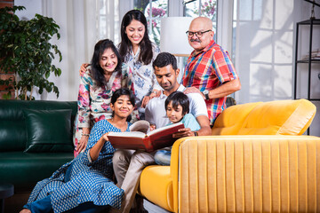 Indian asian kids with parents and grand parents sitting on sofa and watching photos in album or...