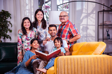 Indian asian kids with parents and grand parents sitting on sofa and watching photos in album or reads book