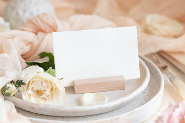 Card near cream tulle fabric on plates close up, copy space, wedding stationery mockup