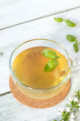Cup of fresh basil tea on wooden table. Hot herbal drink with yellow color. Close-up. Selective focus.