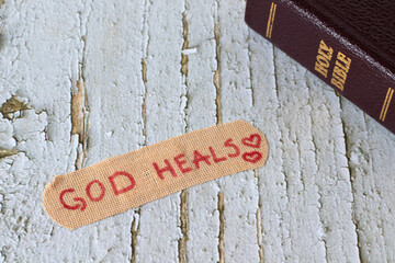 God heals, handwritten text on bandage with closed holy bible book on wooden background. Christian...