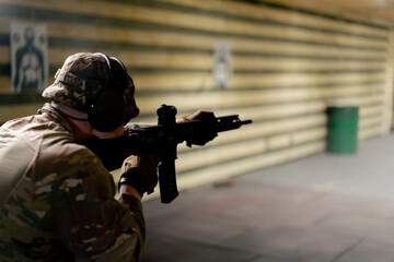 Fototapeta premium In a professional shooting range military man in ammunition makes a shot from a NATO rifle