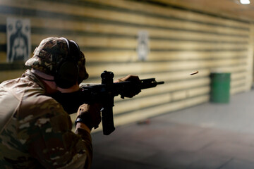 In a professional shooting range military man in ammunition makes a shot from a NATO rifle