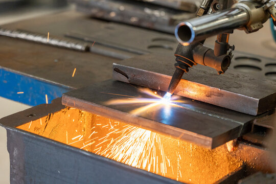 A close-up of a plasma cutting machine slicing through a thick metal plate, with bright sparks and intense heat demonstrating the power of industrial machinery