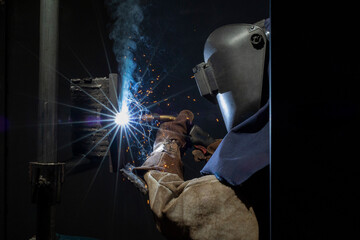 A skilled welder in protective gear works attentively with metal, creating intense sparks while...