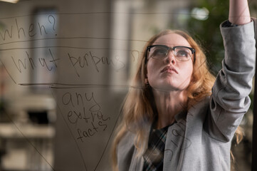 Caucasian woman writing pyramid diagram with questions on glass wall. 