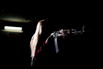 tactical strategy military girl stands with rifle aiming in the dark contrast light back light...