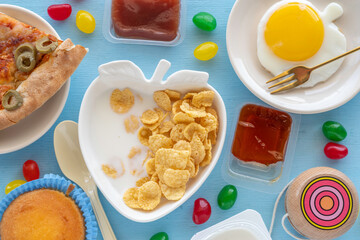 Breakfast ideas for kids. Cornflakes, jam, jelly candies, sunny side up egg, pizza on blue wooden background.