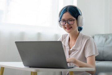 Smiling girl student wear headphone study online with teacher, happy young asian woman learn lecture watch webinar write notes look at laptop sit in home, distant education