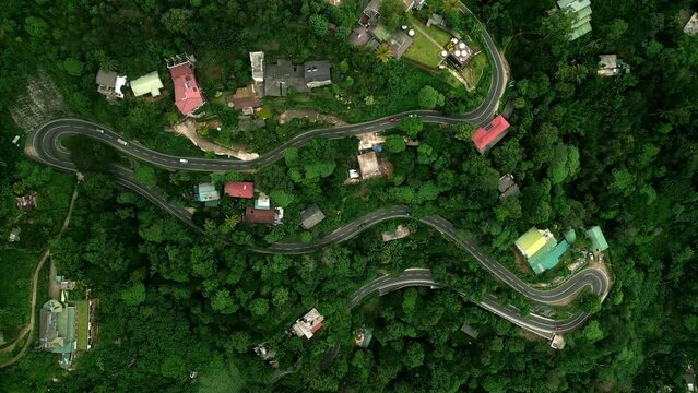 Aerial view over mountain roads weaving through green forest in Sri Lanka. Vehicles navigate tight turns, rural transportation tropical scenery. Scenic route vibrant community colorful houses.