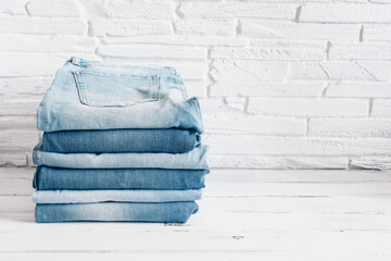 Jeans trousers stack on the background of a white brick wall. Selective focus. Blue denim pants.