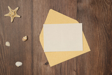 Envelope with blank paper and seashells on wooden background from above. Flat lay, top view