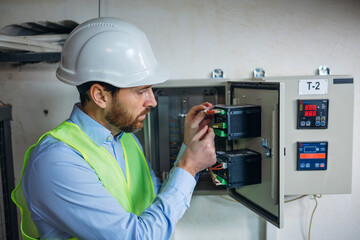 electrician engineers in protective uniform checking voltage control panel screen system at electrical cabinet