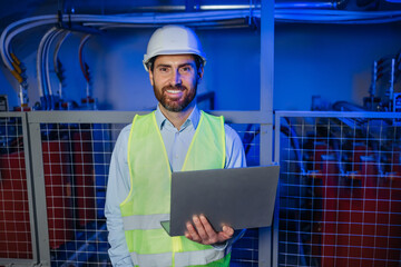 Portrait of Young Professional Engineer / Worker Wearing Safety Vest and Hardhat Smiling on Camera hold laptop